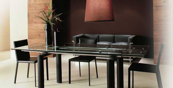 Bauhaus Tisch LC6 umgeben von modernen schwarzen Stühlen. In der Nische des Showroom Ambiente ein schwarzes Le Corbusier Sofa.